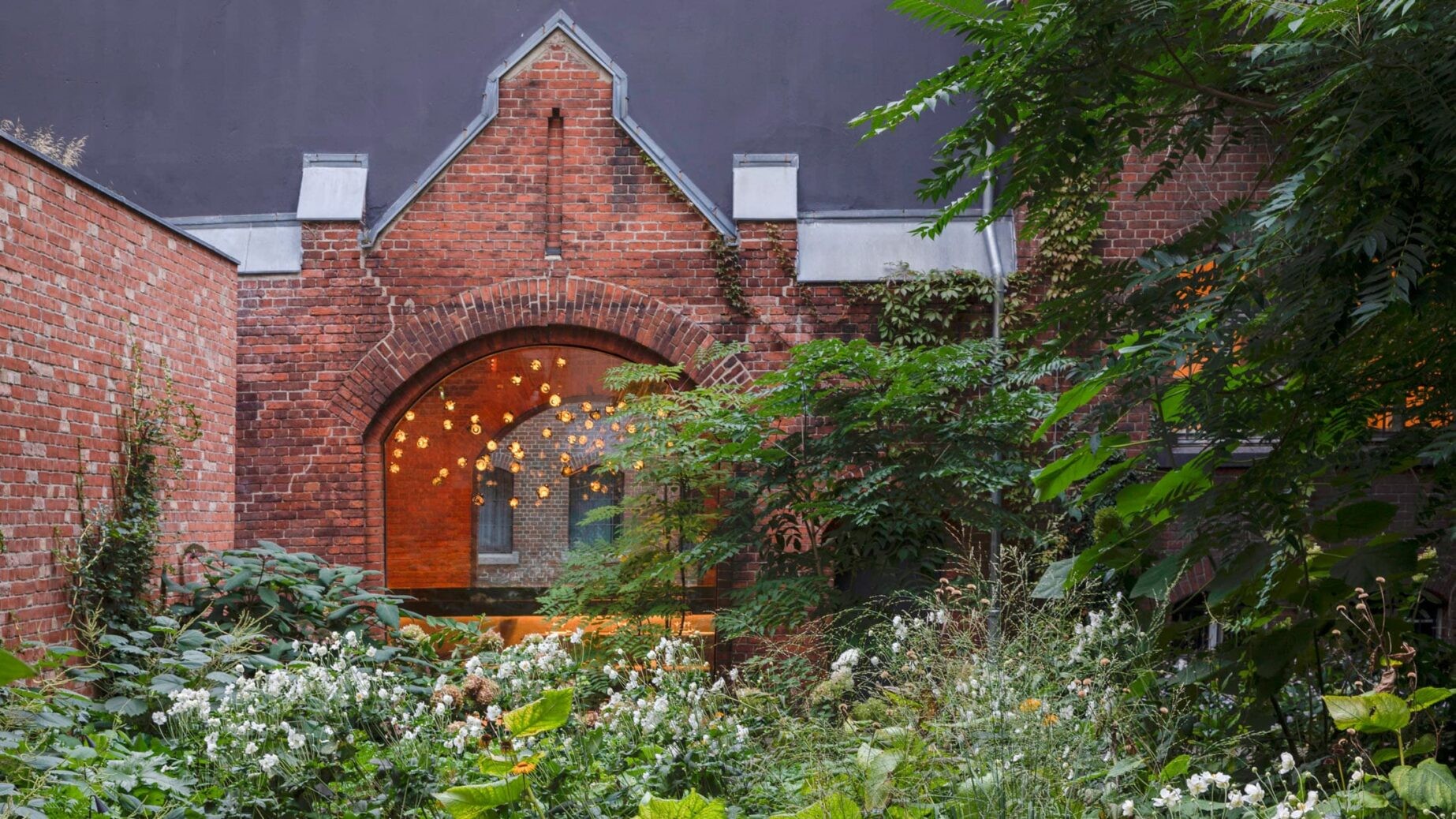 Brick institutional building with tall arched windows facing a planted inner yard